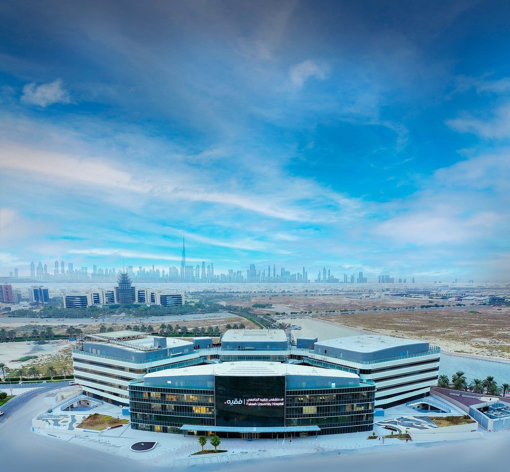 A modern hospital in Dubai seen from the air, with the city skyline behind.
