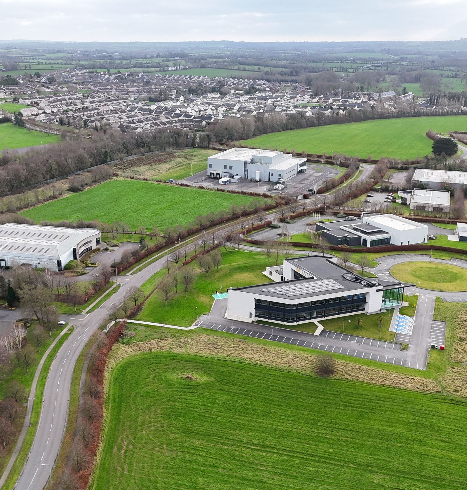 Aerial view of a business park: flat-roofed buildings, access roads and open grass.