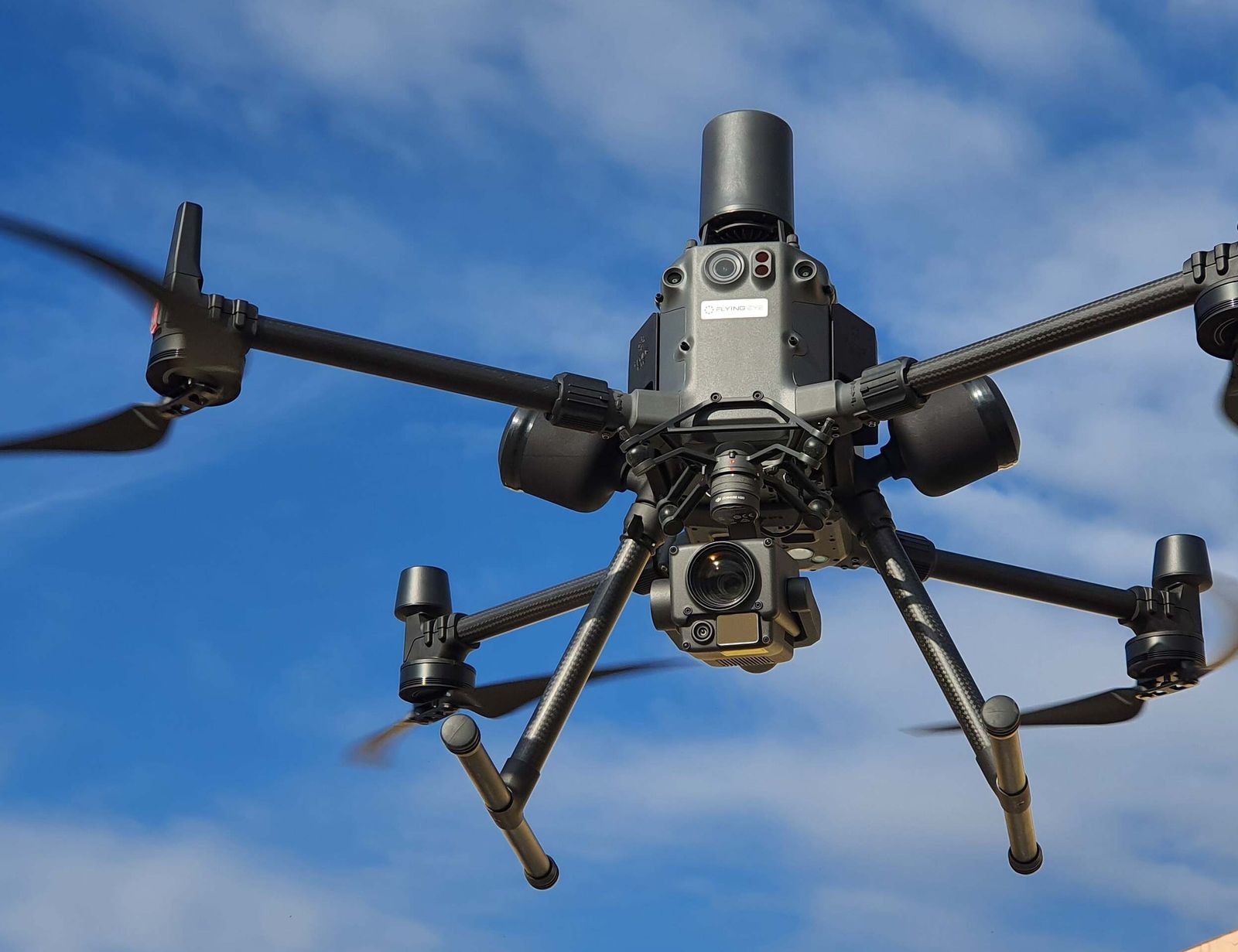 A DJI Matrice 300 inspection drone hovering against a cloudy blue sky.