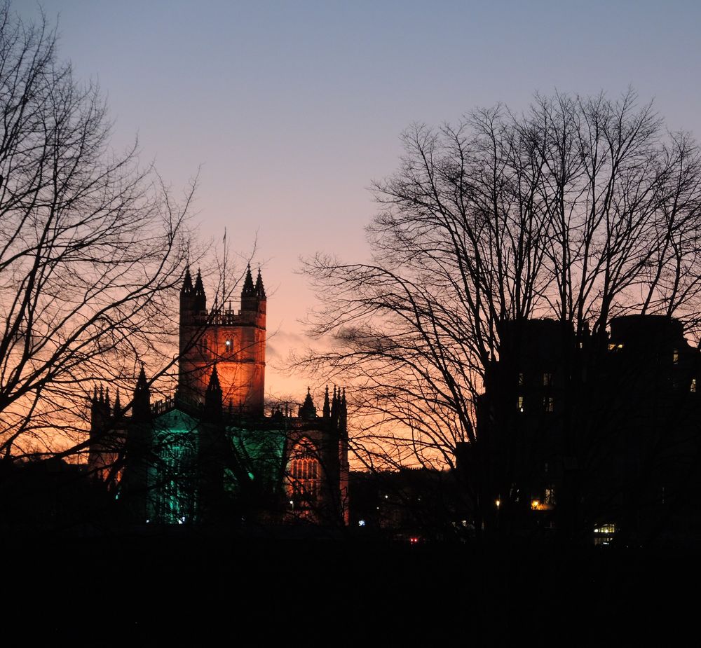 Bath Abbey and the roofline of the city centre in silhouette at dusk.
